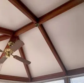 Conservatory ceiling with white panels, dark wood effect beams and a brass ceiling fan